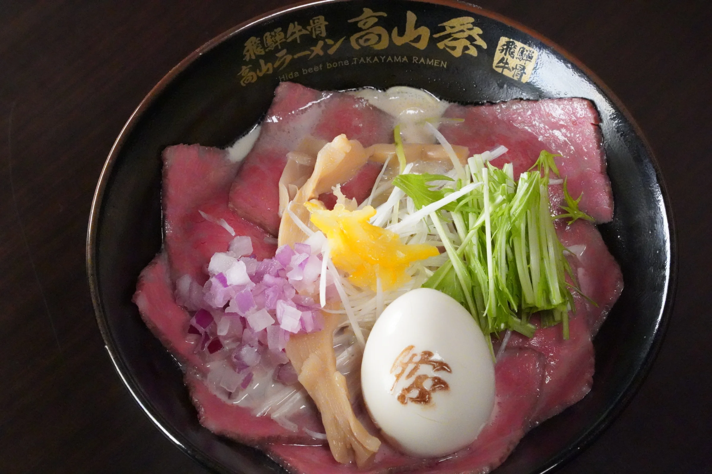 Paitan Roast Beef MATSURI. A bowl completely covered in Hida beef roast beef, topped with a seasoned soft-boiled egg branded with the MATSURI character.